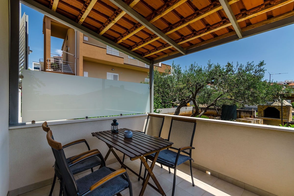 A balcony with a wooden table and chairs, a view of neighboring buildings, and a clear sky.