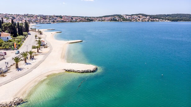 Eine Küstenstadt mit einem Sandstrand, klarem blauen Wasser und einer Parallelstraße entlang der Küste.