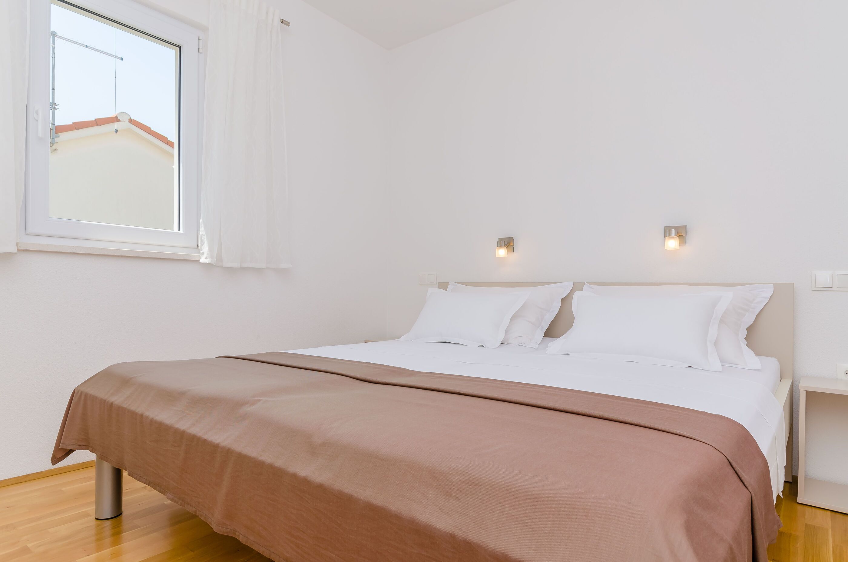 Une chambre à coucher au style minimaliste, avec un lit simple, des murs blancs et une fenêtre avec des rideaux.