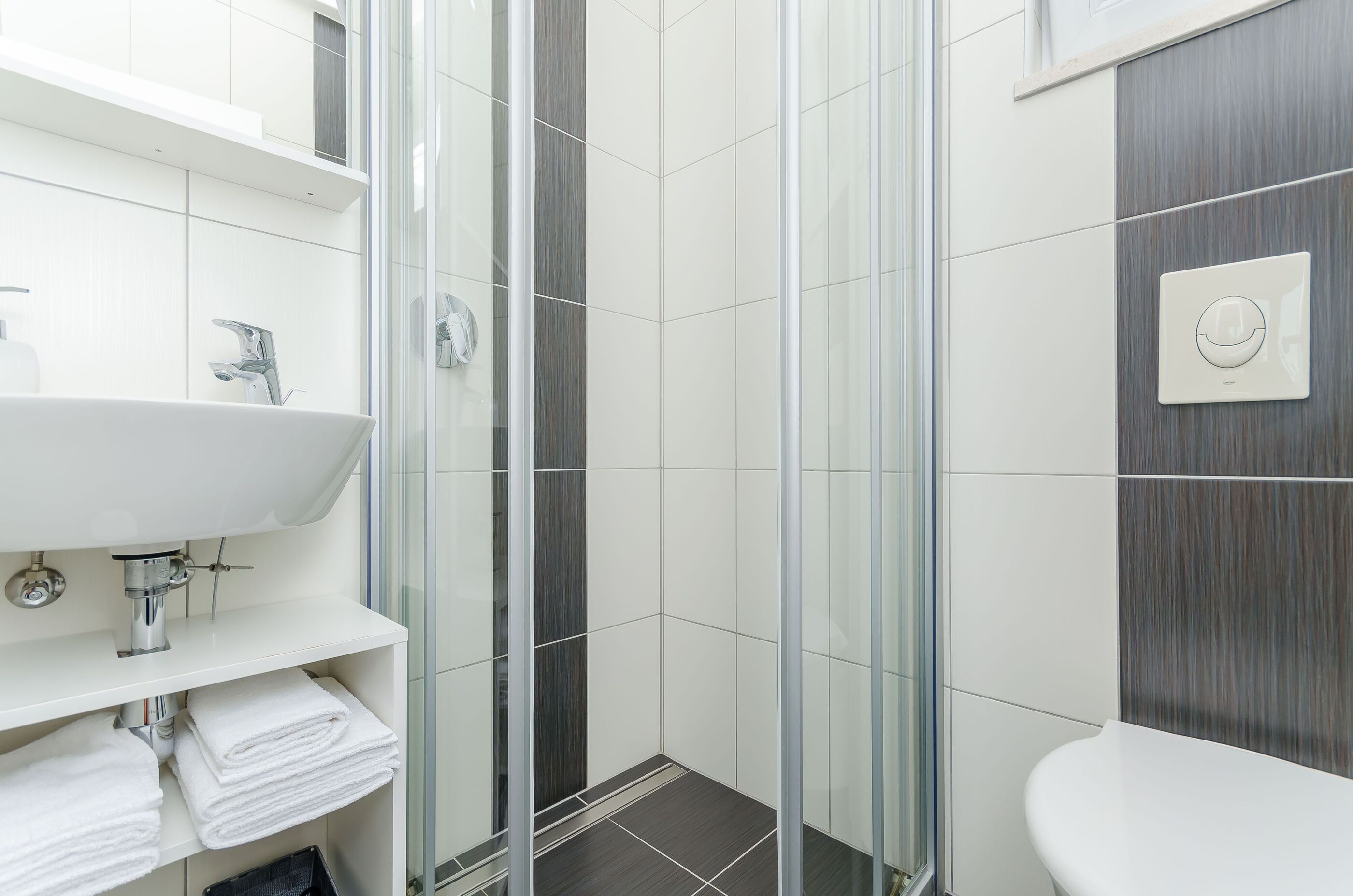 A modern bathroom with a glass shower enclosure, a white sink, and a towel rack.