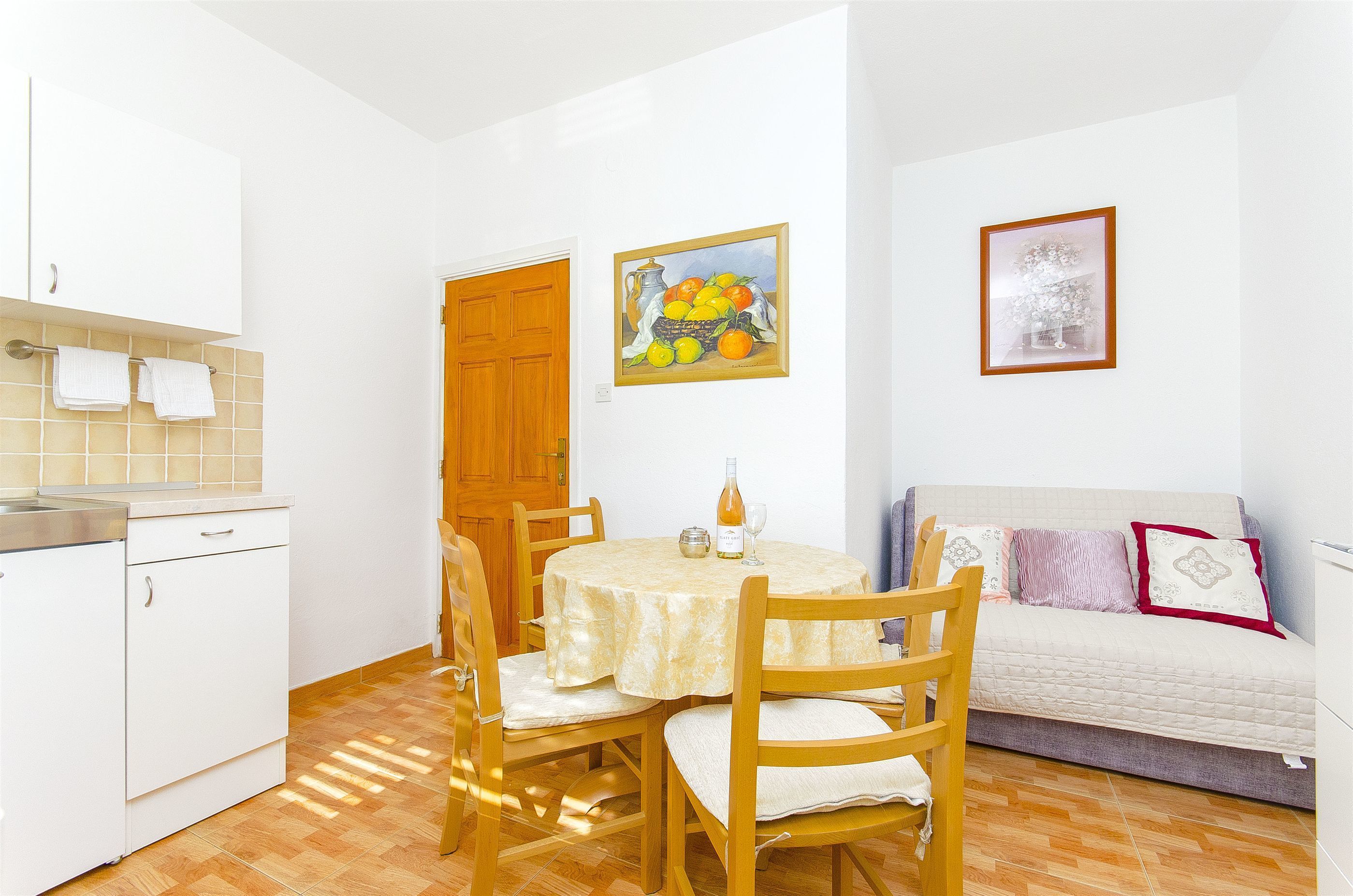 A compact kitchen with a dining table, chairs, a sofa, and a painting on the wall.