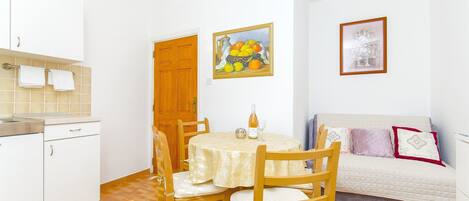A compact kitchen with a dining table, chairs, a sofa, and a painting on the wall.