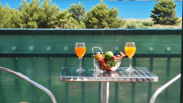 A table with a fruit bowl and two glasses of orange juice, overlooking a scenic coastal view. - Apartments Marija (Trogir)