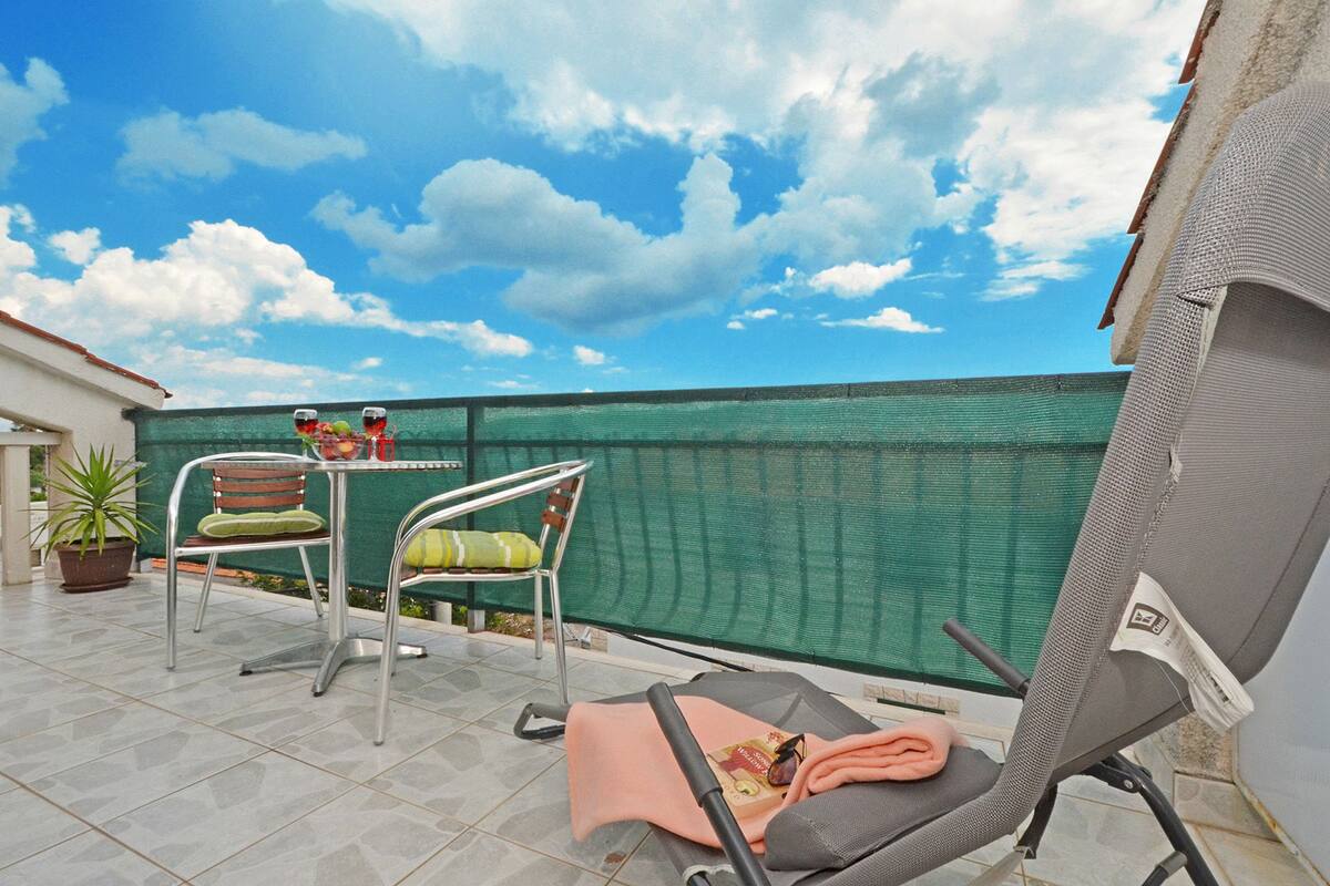 A balcony with two chairs, a table with drinks, and a potted plant.