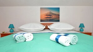 A hotel room with a bed, two pillows, two lamps, and a painting of a mountain. - Apartments Marija (Trogir)