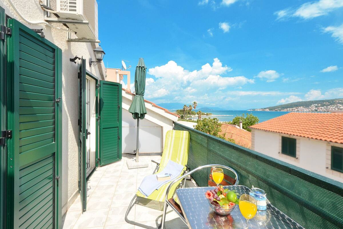 A balcony with a table set for two, a chair, and a green umbrella.