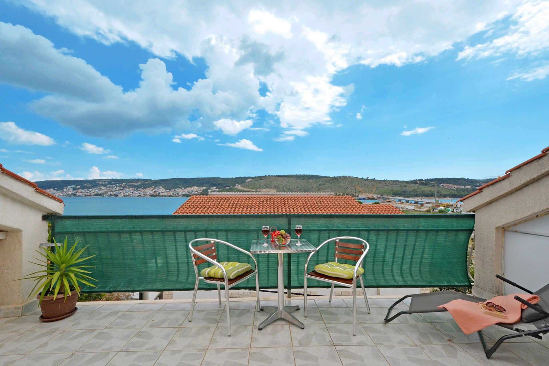 A terrace with two chairs and a table, overlooking a coastal town and hills.