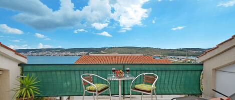 A terrace with two chairs and a table, overlooking a coastal town and hills.