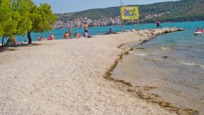 A pebble beach with people sunbathing and a jet ski in the water. - Apartments Marija (Trogir)