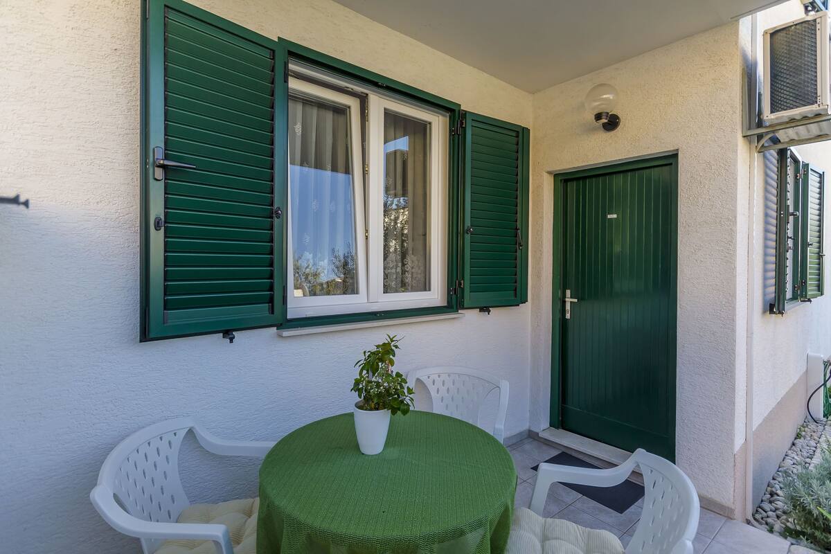 A small outdoor seating area with a round table and chairs, a potted plant, and a green door.