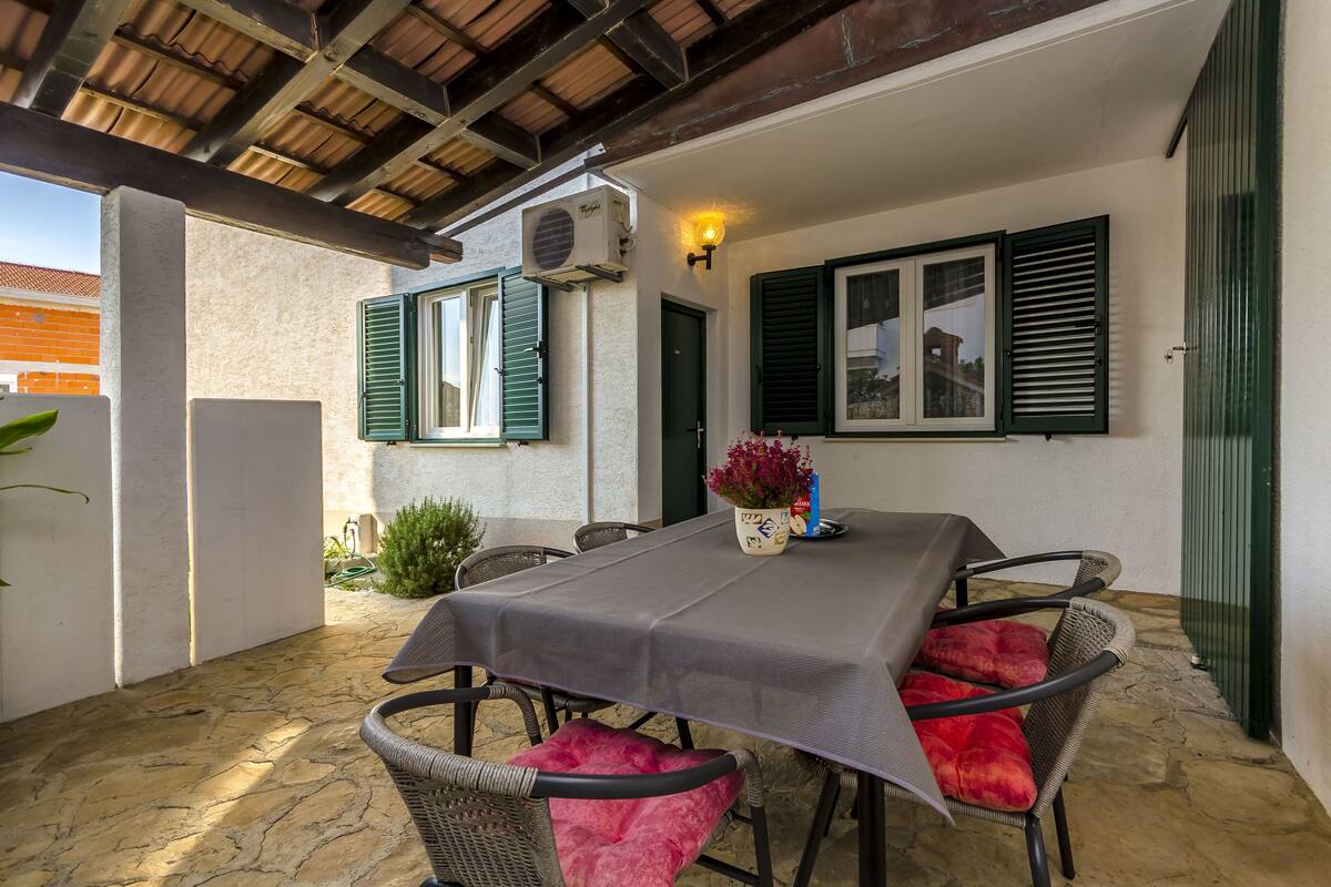 An outdoor patio with a table and chairs, an air conditioning unit, and a wall-mounted light fixture.