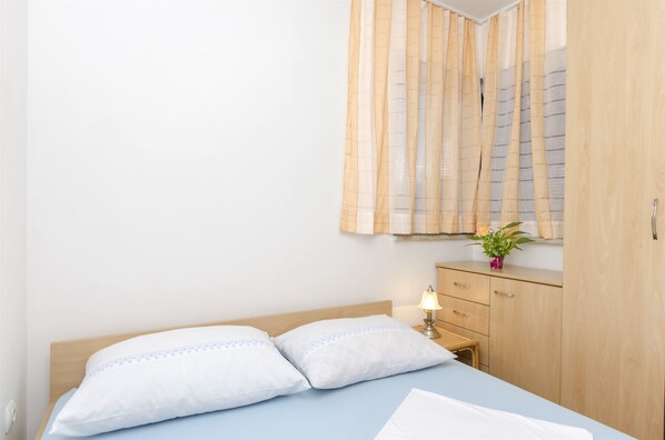 A bedroom with a bed, bedside table, lamp, wooden wardrobe, and a window with curtains.