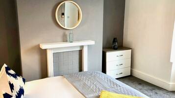 Una habitación de hotel con cama, mesita de noche, espejo y un pequeño armario.