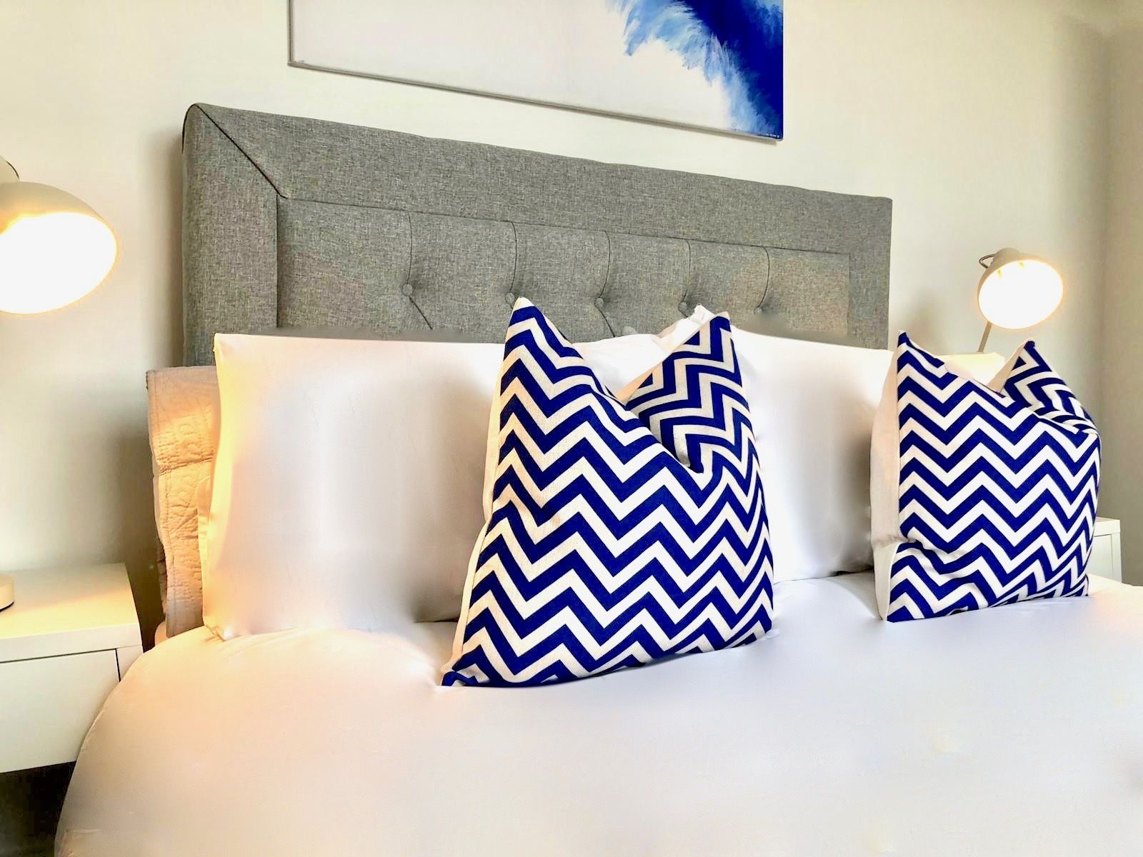 Una cama con ropa de cama blanca y dos almohadas azul y blanco diseño en zigzag.