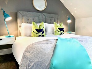 Ein modernes Schlafzimmer mit grauem gepolsterten Kopfteil, einem runden Spiegel und zwei Nachttischlampen.