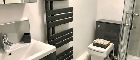 A modern bathroom with a white sink, black storage cabinets, a black towel rack, a toilet, and a glass shower enclosure.