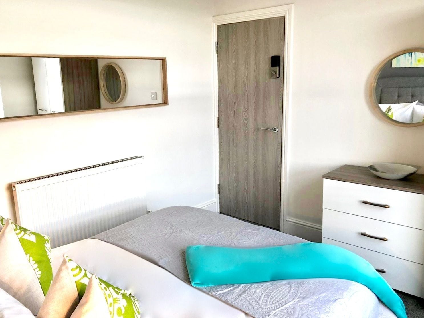 A bedroom with a bed, a bedside table with a bowl, a dresser, a door, and a mirror on the wall.