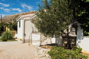 A white building with a staircase leading to a door, surrounded by greenery and a clear sky.