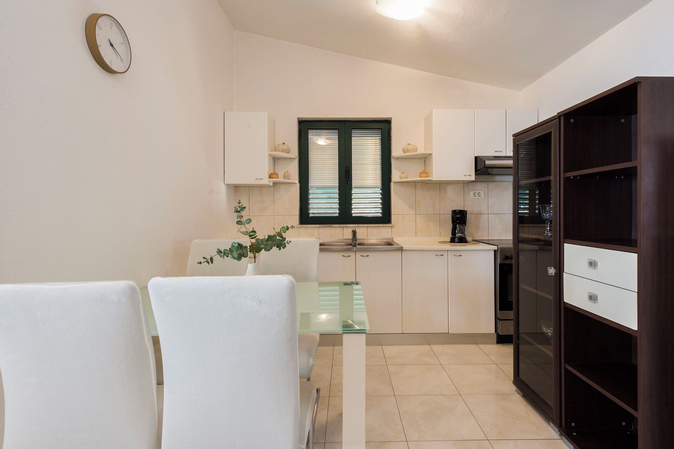 A compact kitchen with white cabinets, a coffee machine, and a dining area with a glass table and chairs.