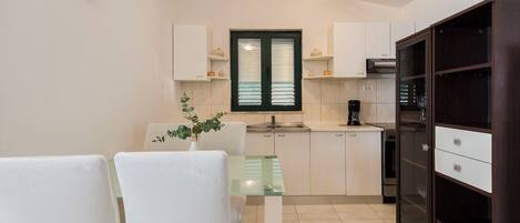 A compact kitchen with white cabinets, a coffee machine, and a dining area with a glass table and chairs.