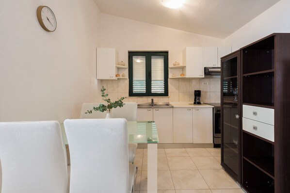 A compact kitchen with white cabinets, a coffee machine, and a dining area with a glass table and chairs.