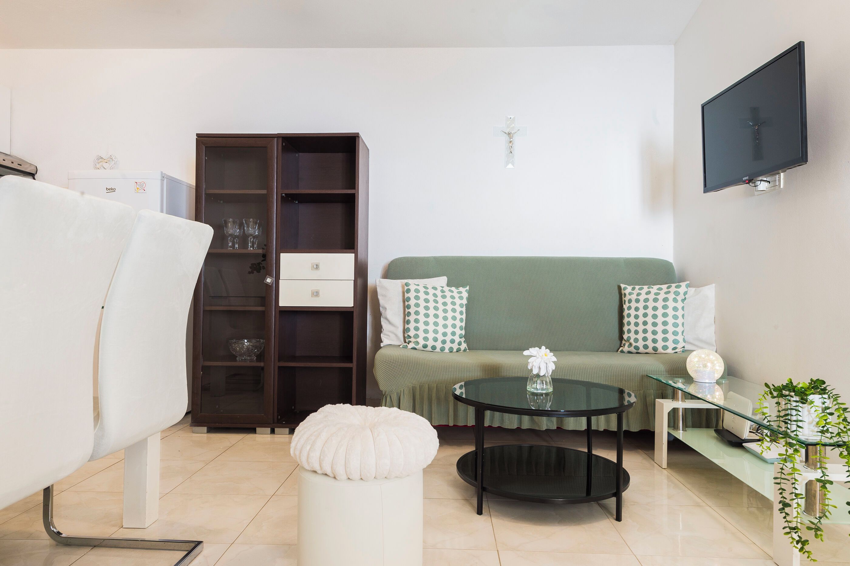 A living room with a sofa, ottoman, glass coffee table, and a cabinet with glass doors.