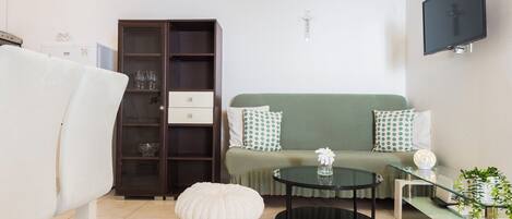 A living room with a sofa, ottoman, glass coffee table, and a cabinet with glass doors.