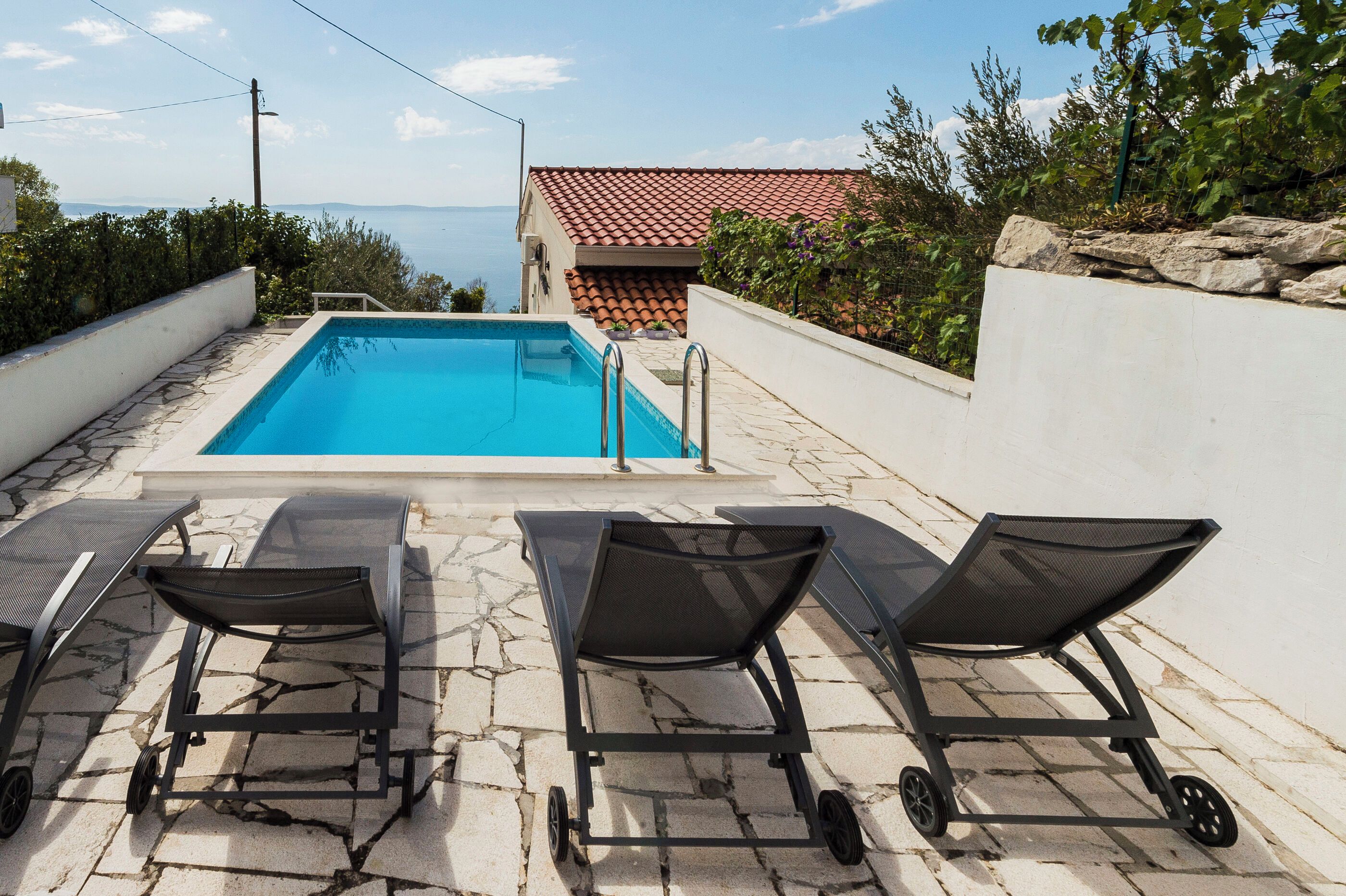 Una piscina con solarium piastrellato, due sdraio e vista sul mare.