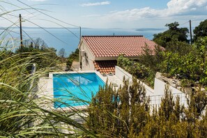 A residential property with a swimming pool, a red-tiled roof, and a view of the sea.