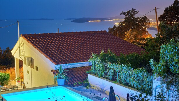 Une maison avec une piscine, un toit recouvert de tuiles rouges et une vue sur la mer.