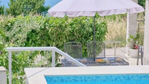 Un espace aménagé au bord de la piscine, avec une table, un parasol et des sièges.