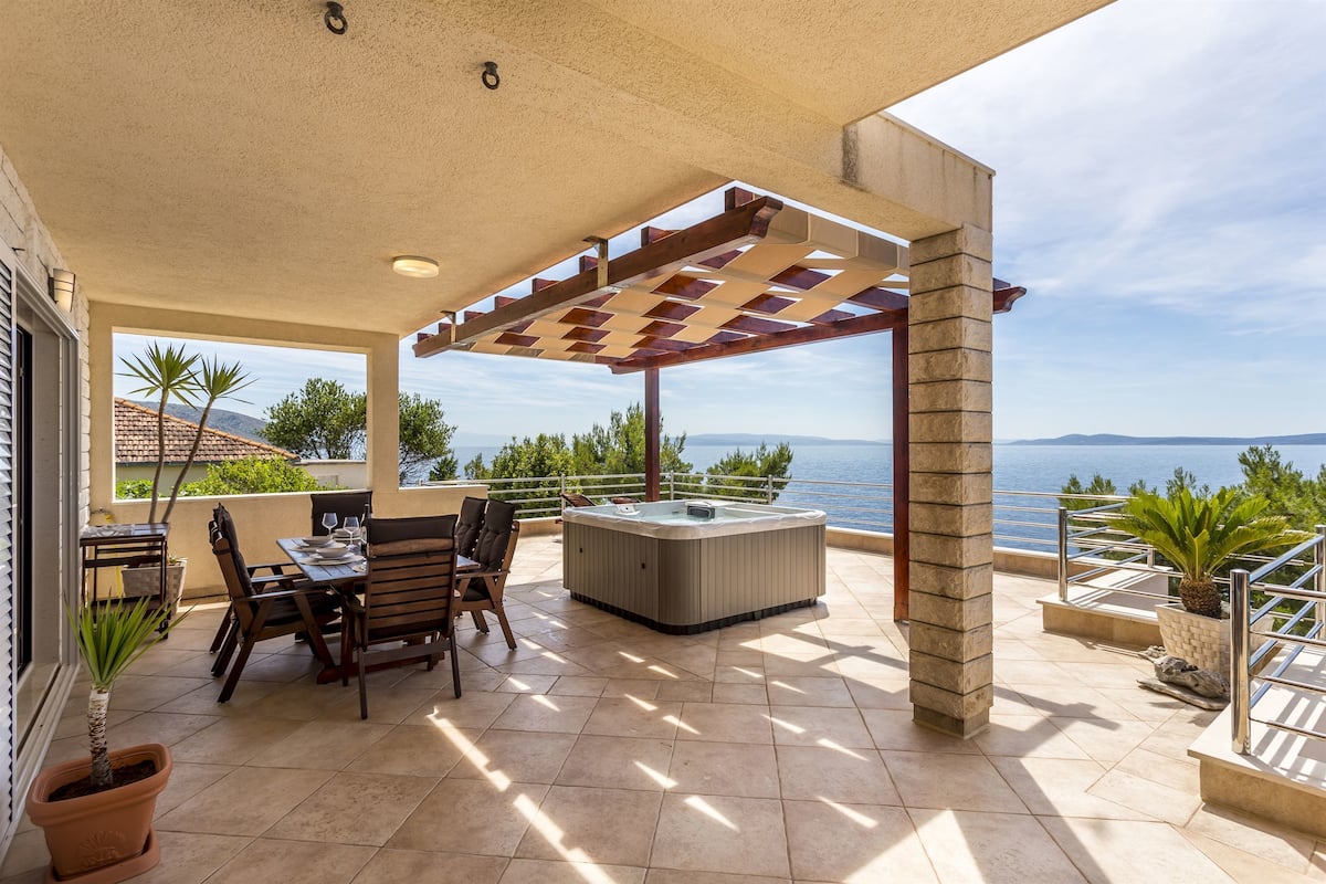 Une terrasse extérieure couverte avec un jacuzzi, un espace salon et une vue sur la mer.