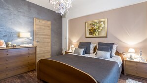 A bedroom with a large bed, wooden dresser, nightstands, a chandelier, and a floral painting on the wall. - Apartment Paradise View (Okrug Gornji)