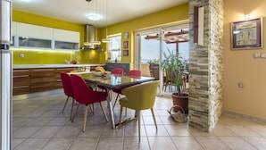 A bright kitchen with yellow walls, a dining table with red and yellow chairs, and a view through large windows. - Apartment Paradise View (Okrug Gornji)