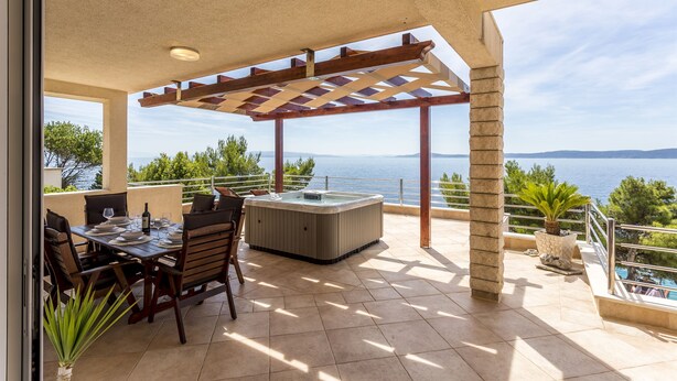 An outdoor patio with a wooden pergola, a hot tub, and a dining area with chairs and a table set for two. - Apartment Paradise View (Okrug Gornji)