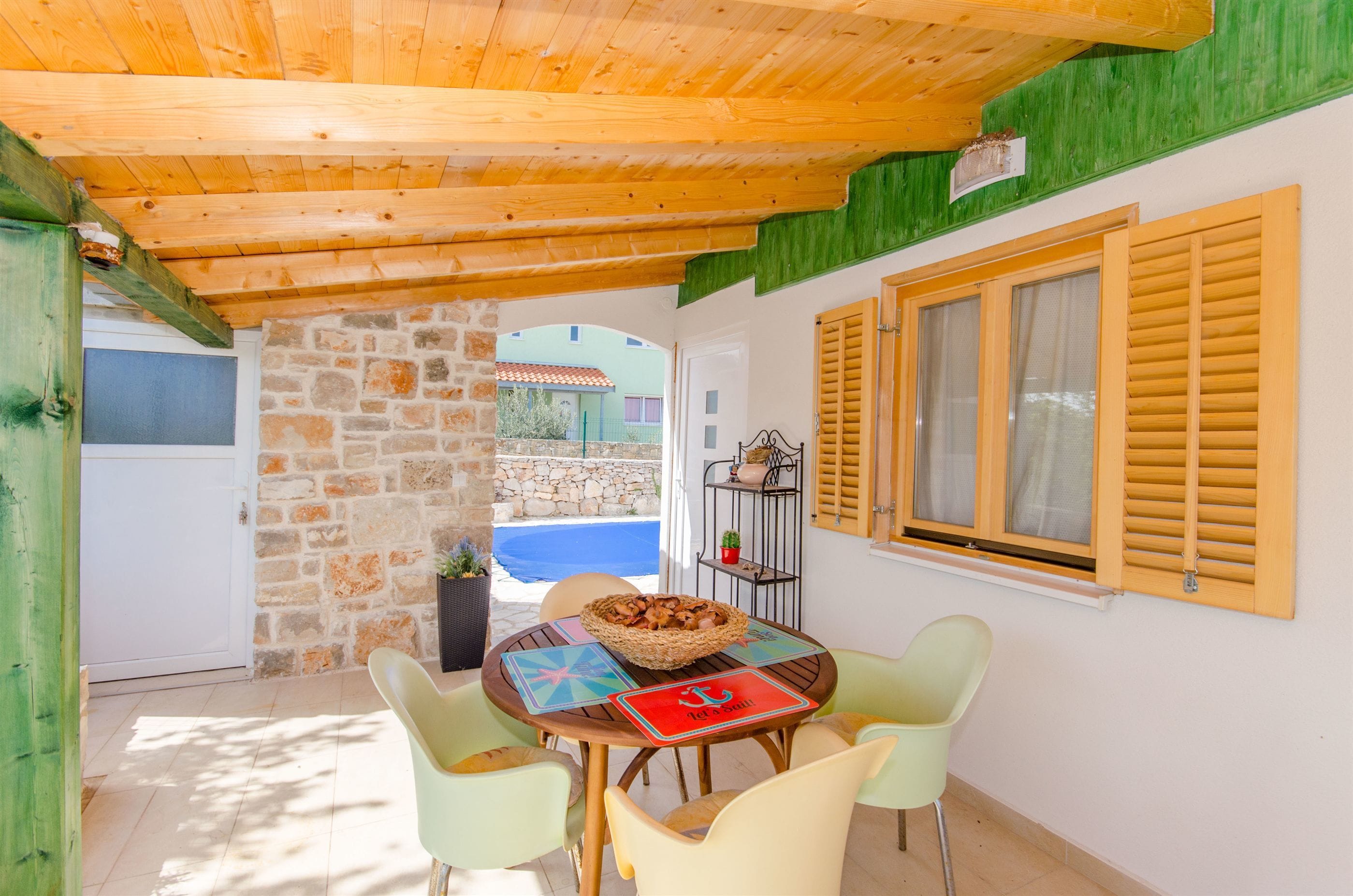 Un comedor con pared de piedra, techo de madera y vista a una piscina.