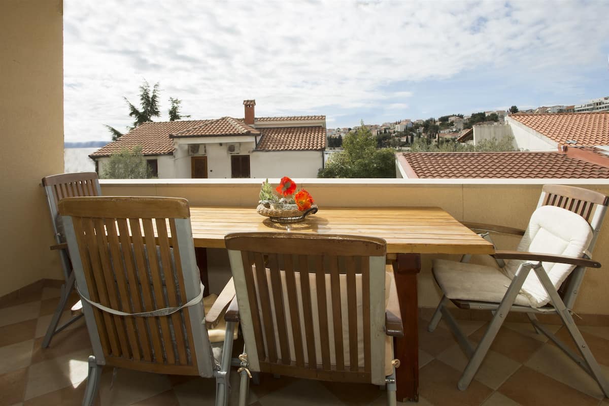 A balcony with a wooden table and two chairs, a flower vase, and a view of houses and trees.
