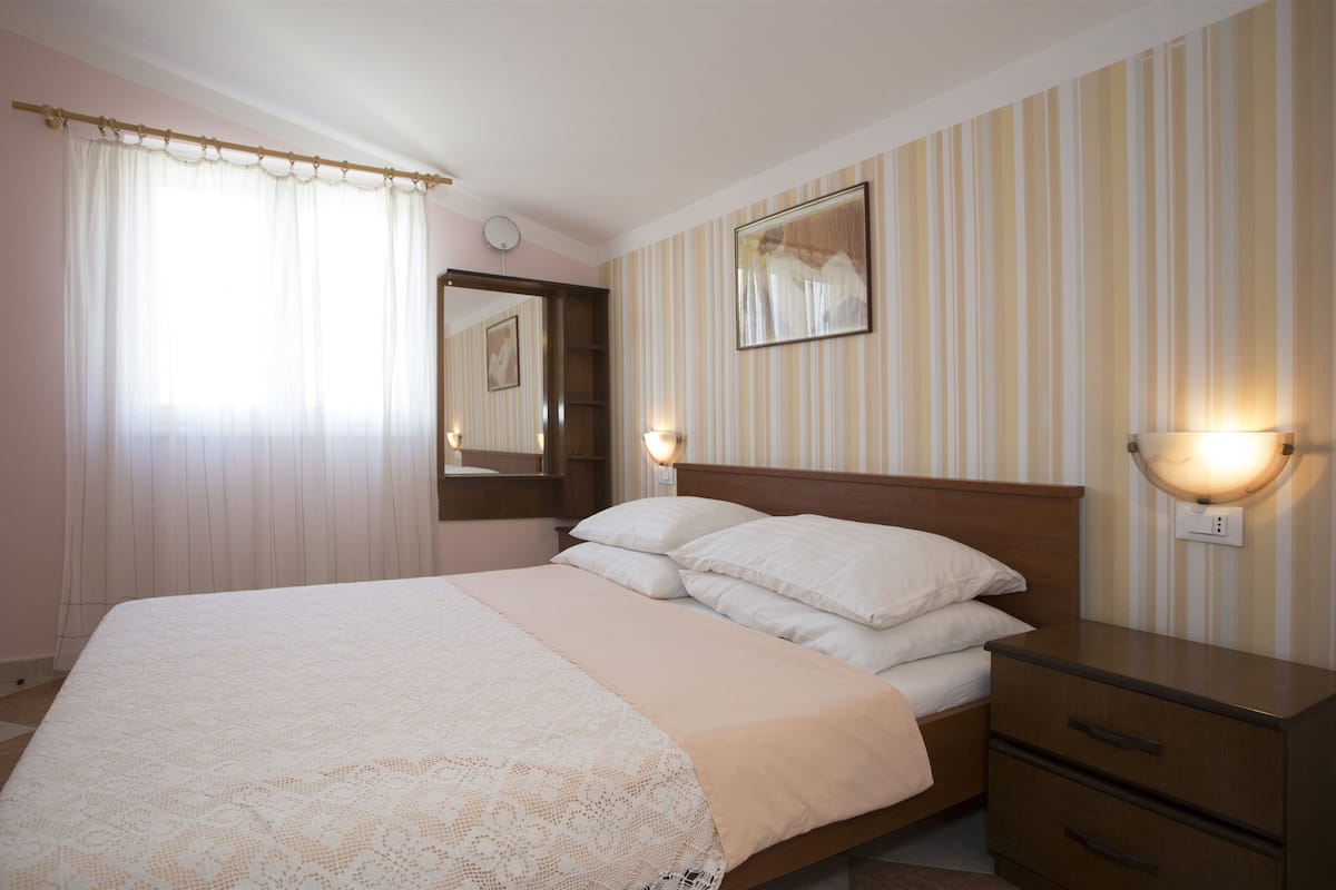 A bedroom with a large bed, bedside tables, a mirror, and striped wallpaper.