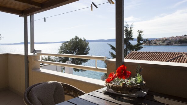 Un balcon avec vue sur la mer, un panier en osier rempli de fleurs et une chaise en osier.