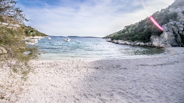 Ein Strand mit klarem Wasser, einem Boot und felsigen Klippen.