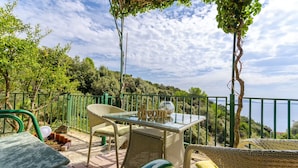 Eine Terrasse mit Korbmöbeln, einem Glastisch und Blick auf das Meer.