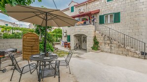 Un patio con una mesa y sillas redondas, una sombrilla y un edificio de piedra con una escalera.