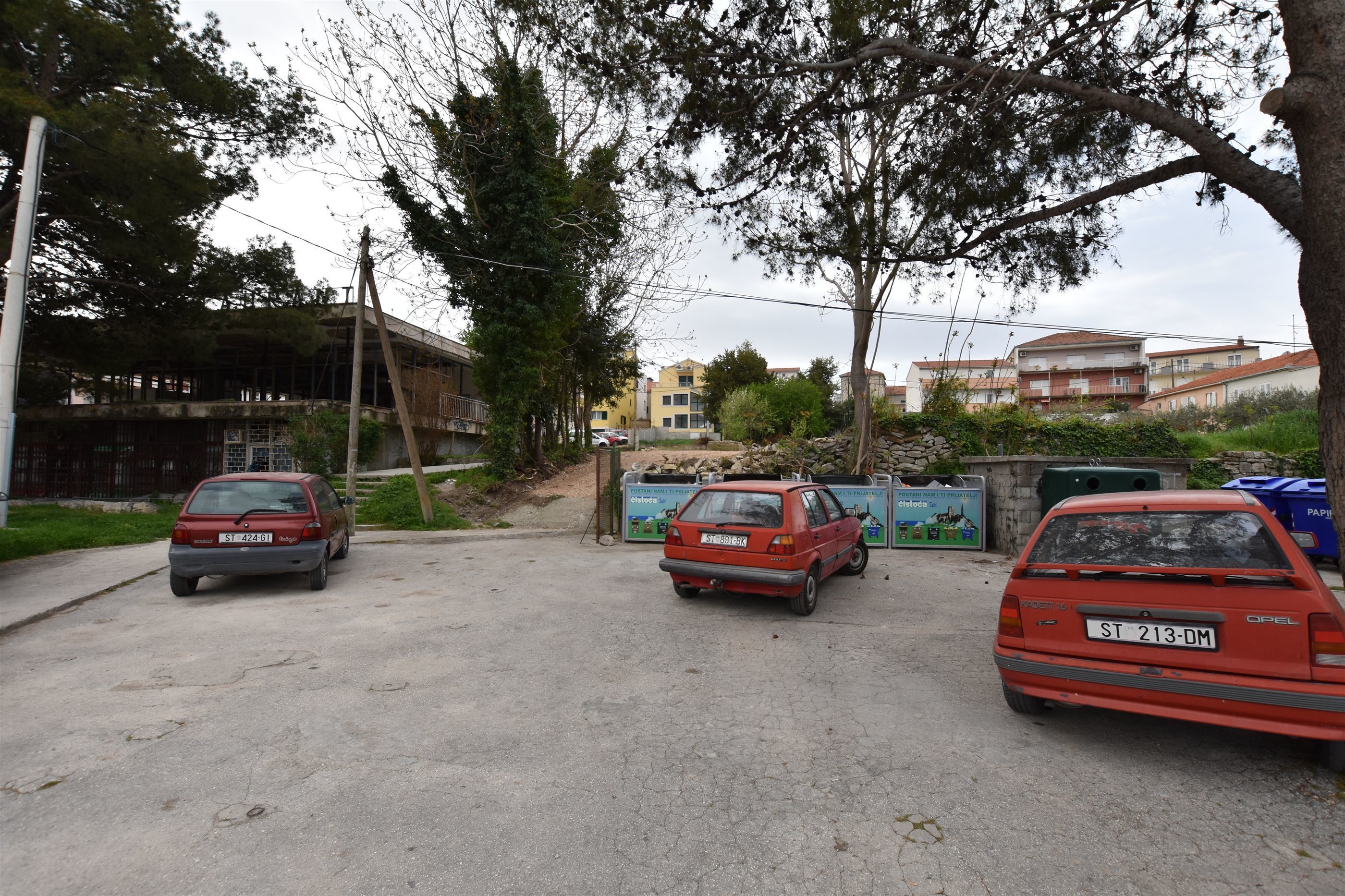 Un estacionamiento con tres coches aparcados, una obra en construcción y edificios residenciales al fondo.