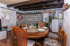 Ein Essbereich mit Steinwand, Holzkstühlen, einem runden Tisch und einer Rettungsboje als Dekoration.