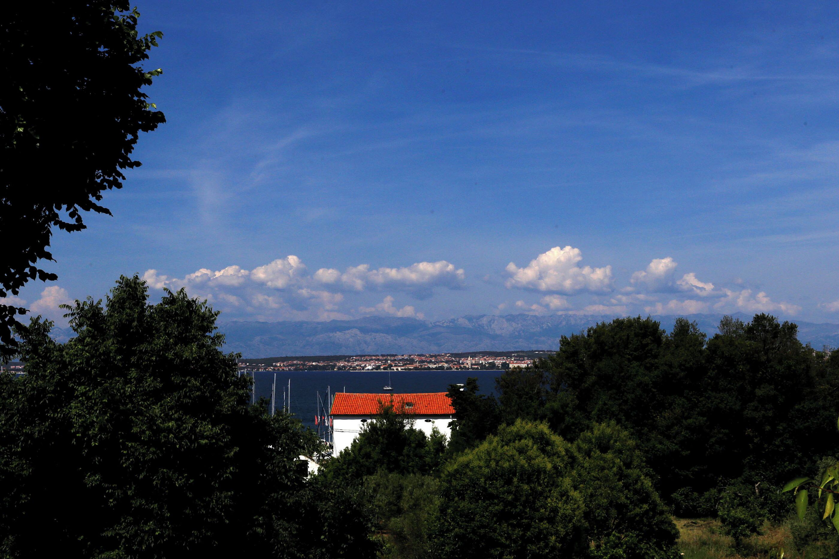 A coastal view with a red-roofed building, a body of water, and distant mountains.