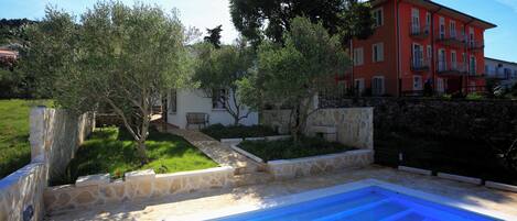 Una piscina con bordes de piedra, un sendero de piedra y un edificio rojo al fondo.