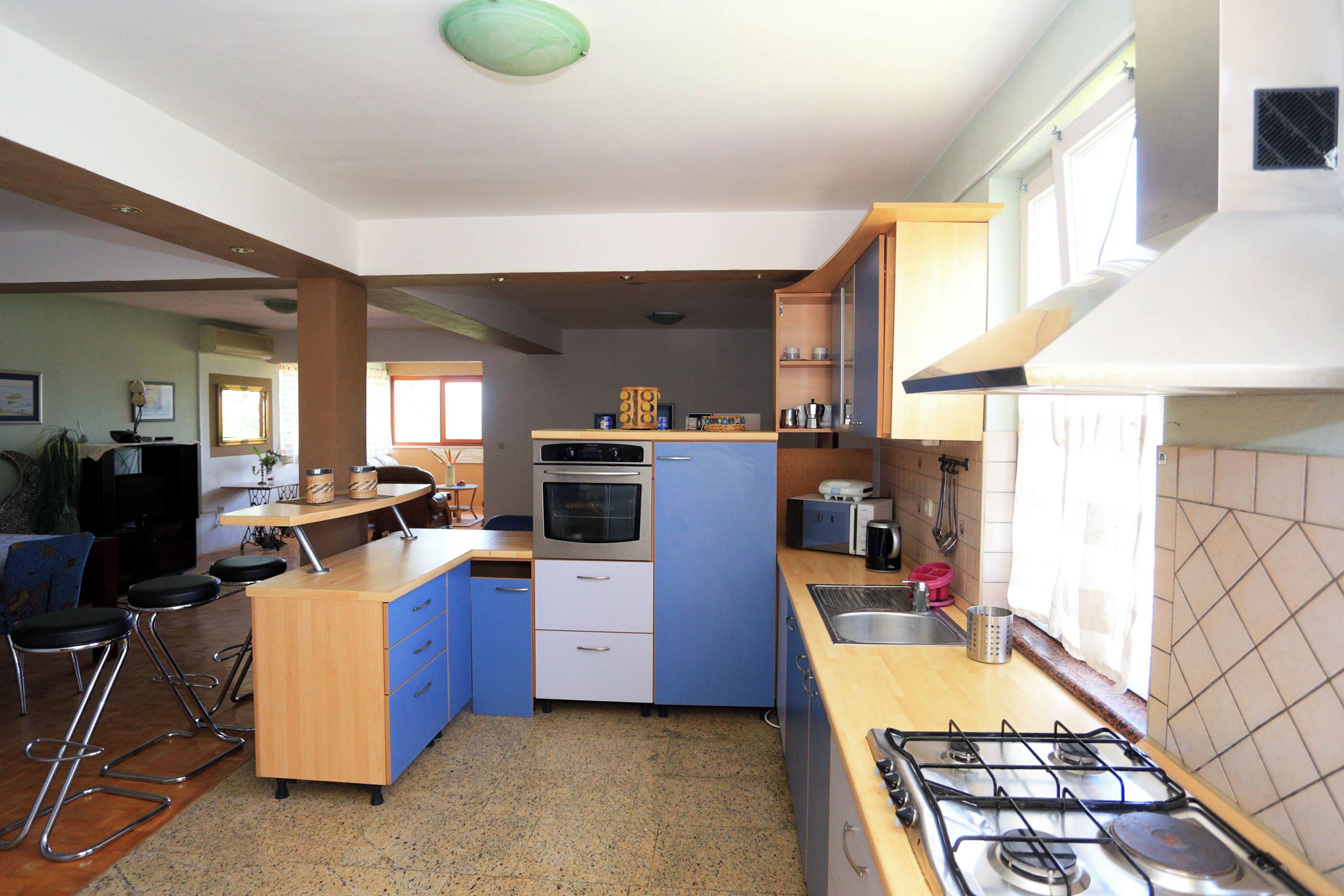 Uma cozinha compacta com fogão a gás, forno e armários azuis. Há banquetas e uma pequena mesa de jantar.
