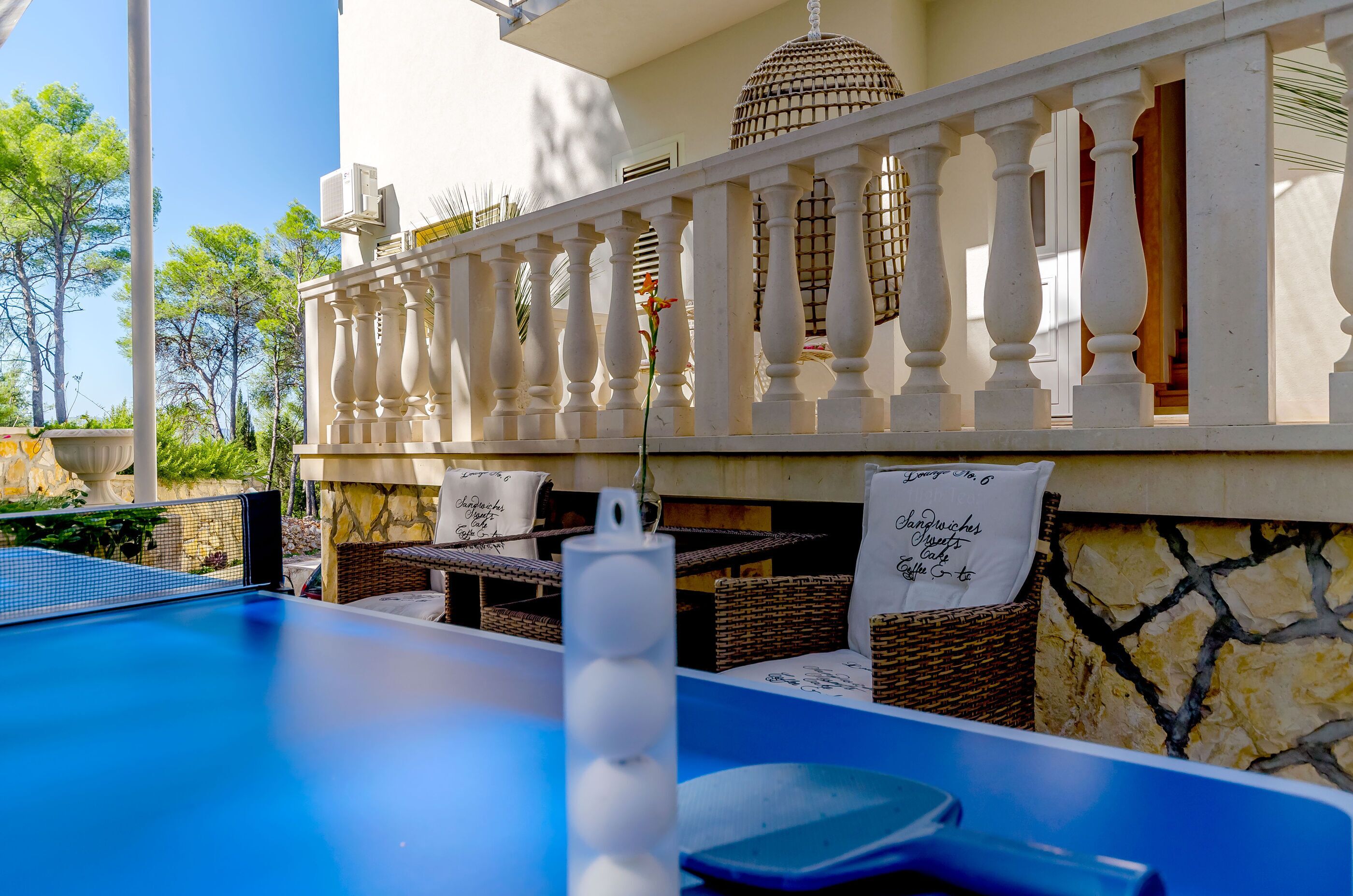 A pool area with a white balustrade, wicker furniture, and a stone wall.