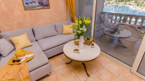 A balcony with a sofa, wicker chairs, a table with flowers, and a view of a marina. - Apartments Vila Jelka (Vrboska)