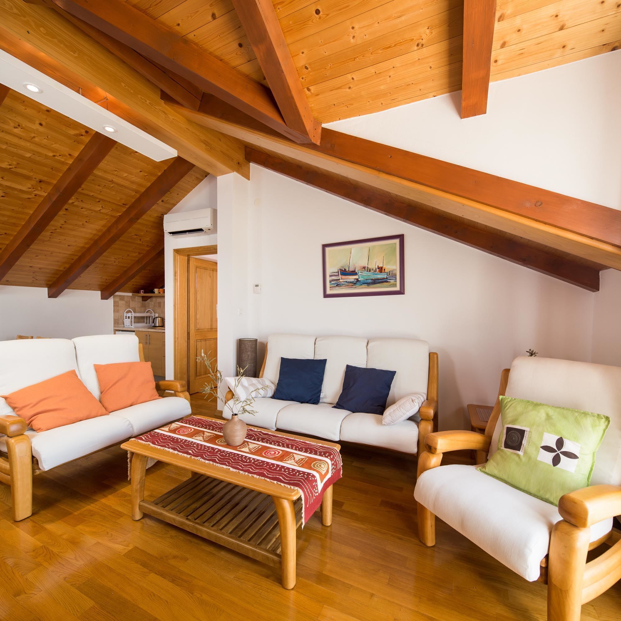 A cozy living room with wooden beams, a white sofa, a wooden coffee table, and a green armchair.